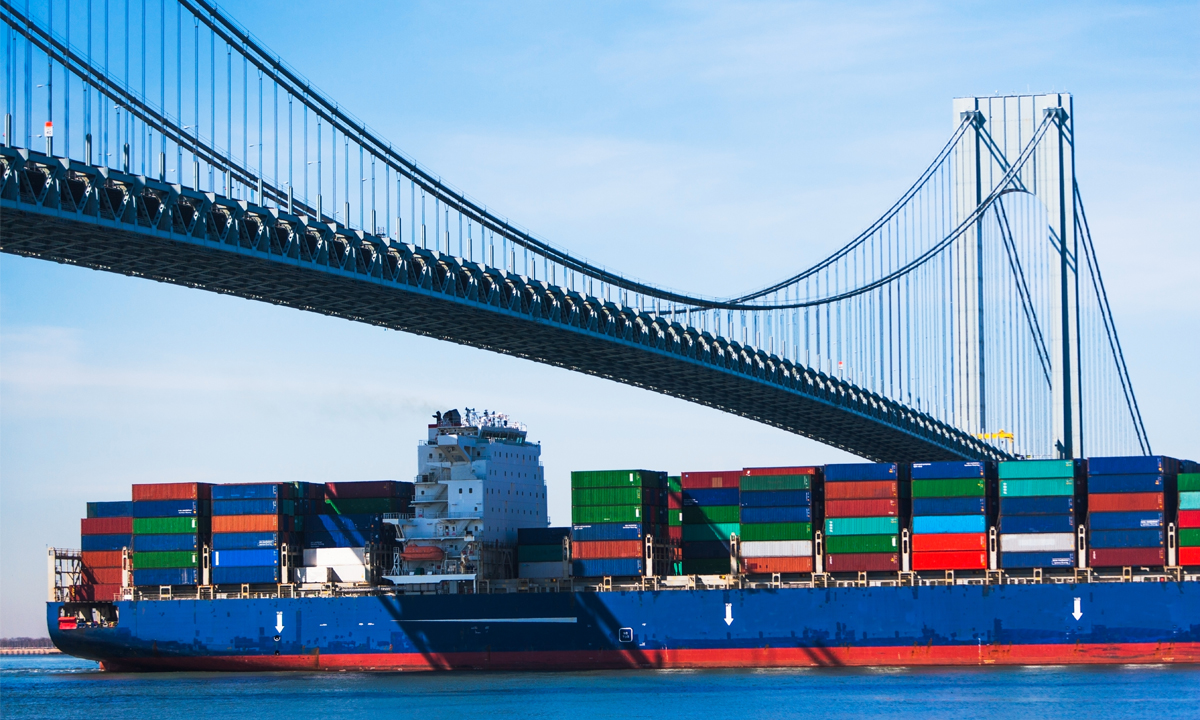 A loaded container ship passes under a bridge